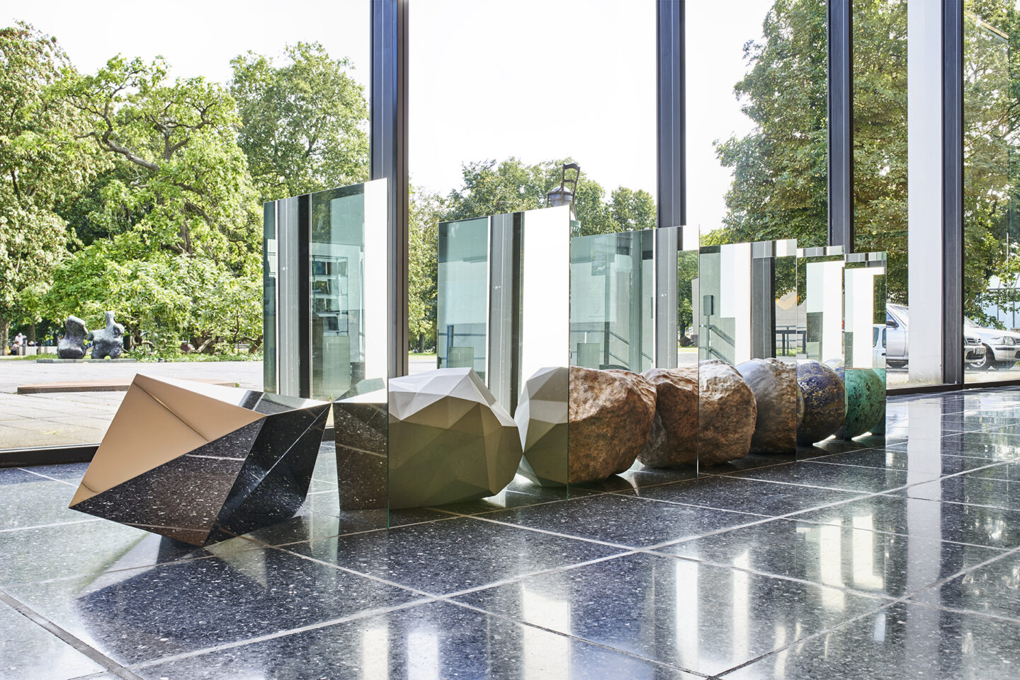 Alicja Kwade im Lehmbruck-Museum, Emergenz, 7 Objekte, (Steine, Kugel, Schale) die in einer Reihe hintereinander am Boden liegen, sind jeweils durch einen doppelseitigen Spiegel voneinander getrennt